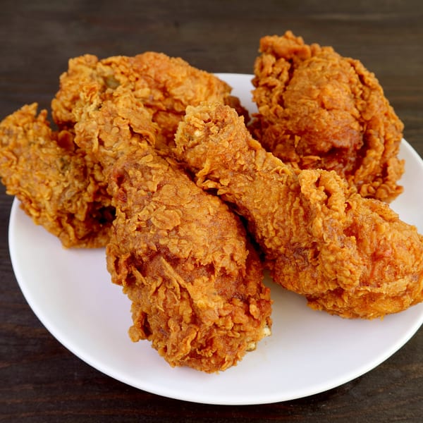 Crispy, golden-brown fried chicken pieces, including drumsticks and thighs, piled on a white plate.