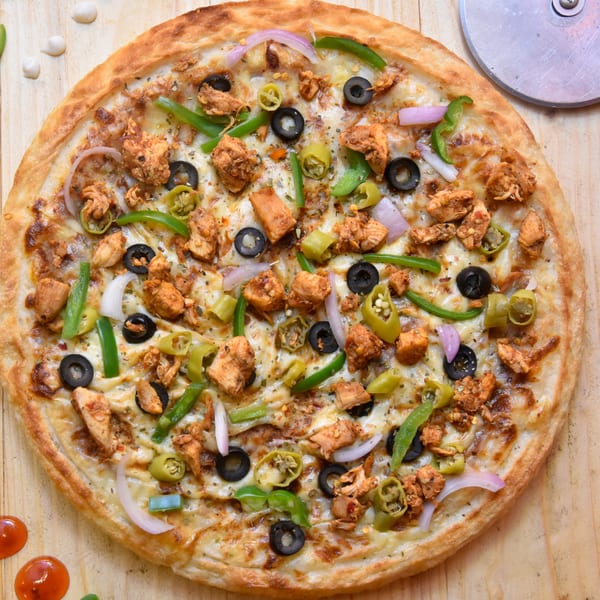 A chicken pizza with black olives, green peppers, and red onions on a wooden table.