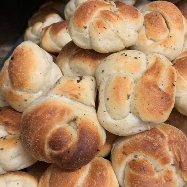 Close-up of a pile of golden-brown garlic knots, sprinkled with herbs, ready to be served.