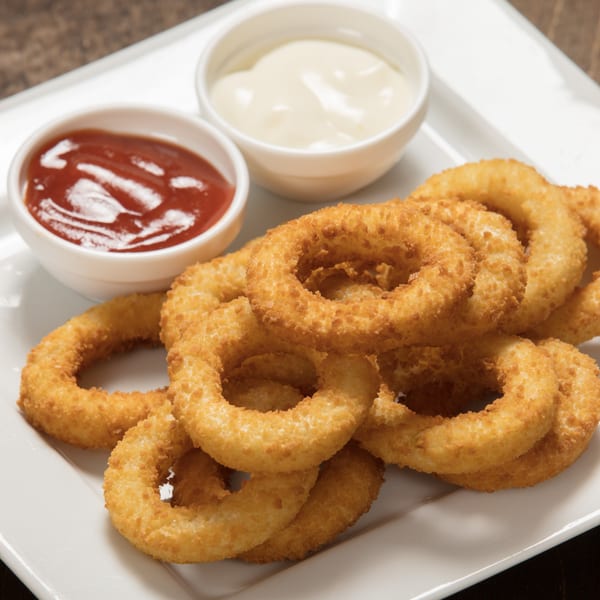 Golden-brown onion rings piled on a white plate with small bowls of ketchup and mayonnaise.